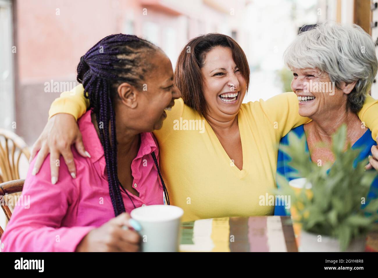 Ältere Freunde aus verschiedenen Rassen treffen sich und unterhalten sich an der Bar im Freien, während sie gemeinsam Kaffee trinken in der Bar Restaurant - konzentrieren Sie sich auf das Gesicht der Frau in der Mitte Stockfoto
