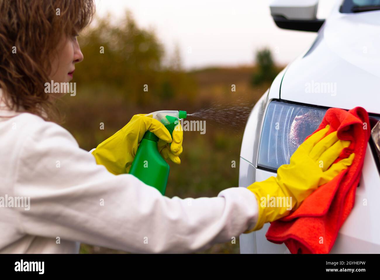 Eine hübsche junge Frau in einem weißen Hoodie und gelben Gummihandschuhen  wischt an einem warmen Herbsttag die Scheinwerfer eines Autos mit einem  leuchtend roten Lappen ab. Selektive Stockfotografie - Alamy