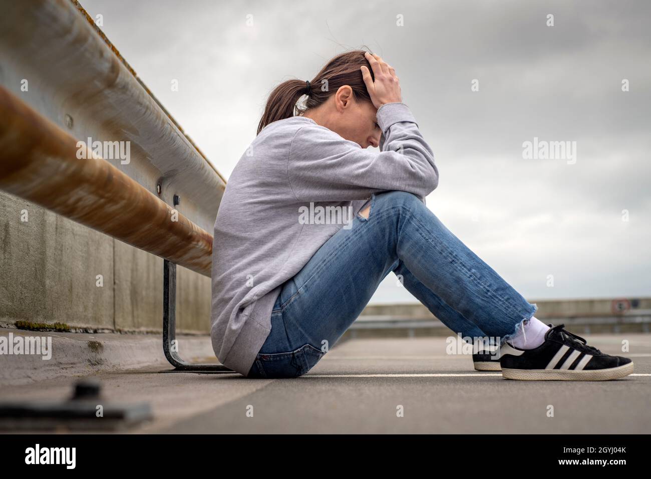 Junge Frau mit dem Kopf in den Händen auf dem Boden sitzend. Konzept für psychische Gesundheit und Beziehungsprobleme. Stockfoto