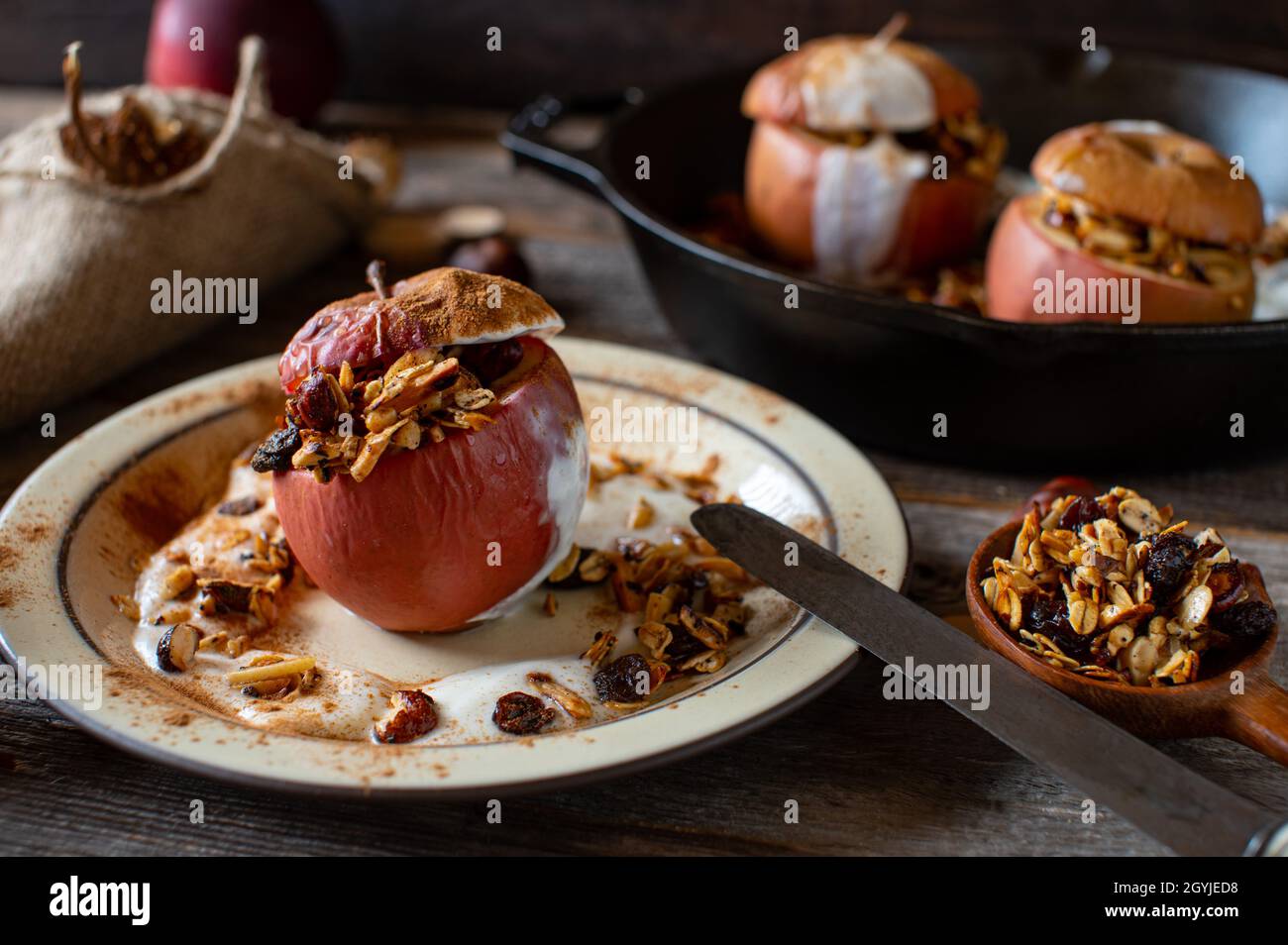 Gesundes Frühstück mit hausgemachtem Müsli, gebackenem Apfel und Joghurt auf rustikalem Holztisch. Köstliches Herbst- und Winterrezept Stockfoto