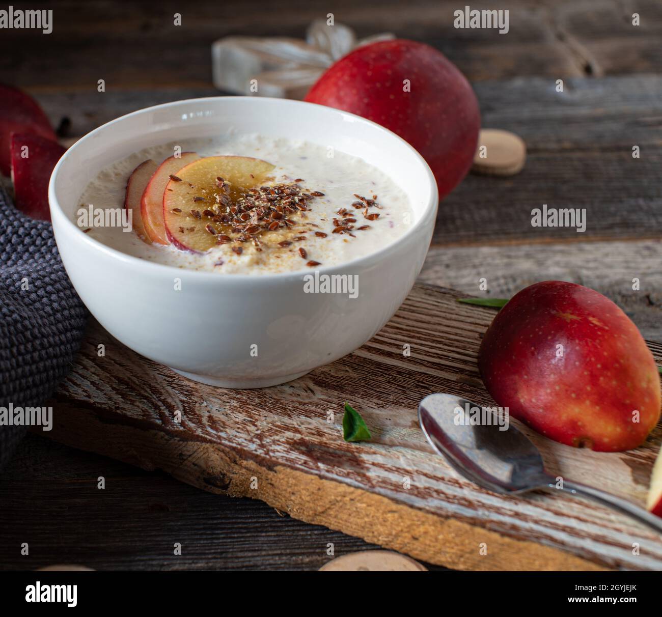Hausgemachter Joghurt, gemischt mit frischen roten Äpfeln, serviert mit Leinsamen in einer Schüssel auf einem Holztisch. Gesundes glutenfreies und kohlenhydratartiges Frühstück oder Snack Stockfoto