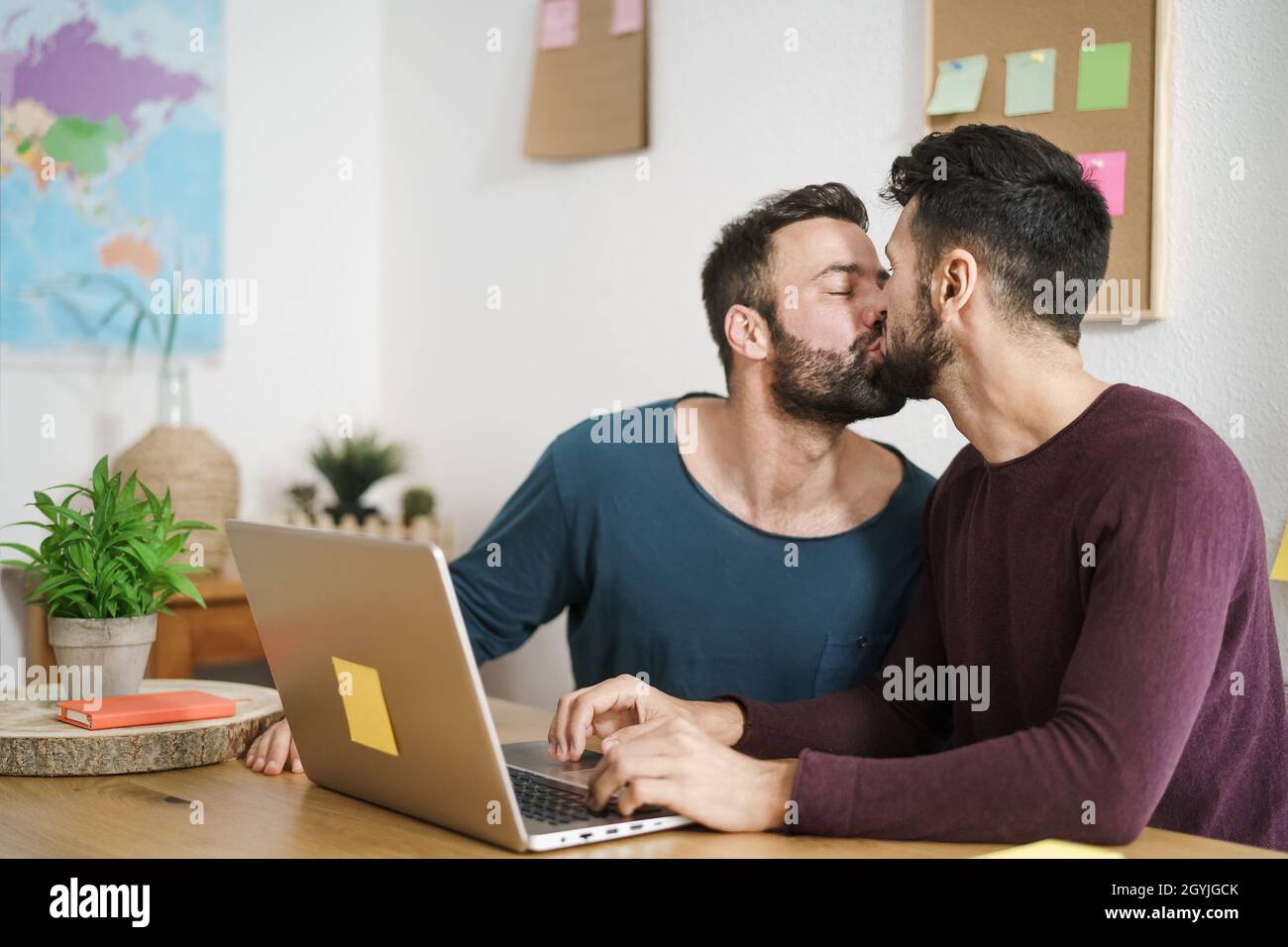 Glücklich schwule Paar küssen während mit Laptop im Wohnzimmer zu Hause - LGBT Liebe und Technologie-Konzept Stockfoto