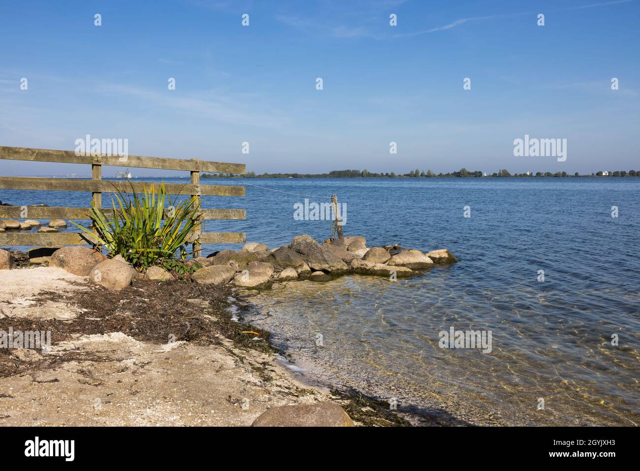 Küste Holländischer See IJmeer bei Muiden mit Holzzaun und Steinen und Blick auf die gegenüberliegende Seite Flevoland Stockfoto