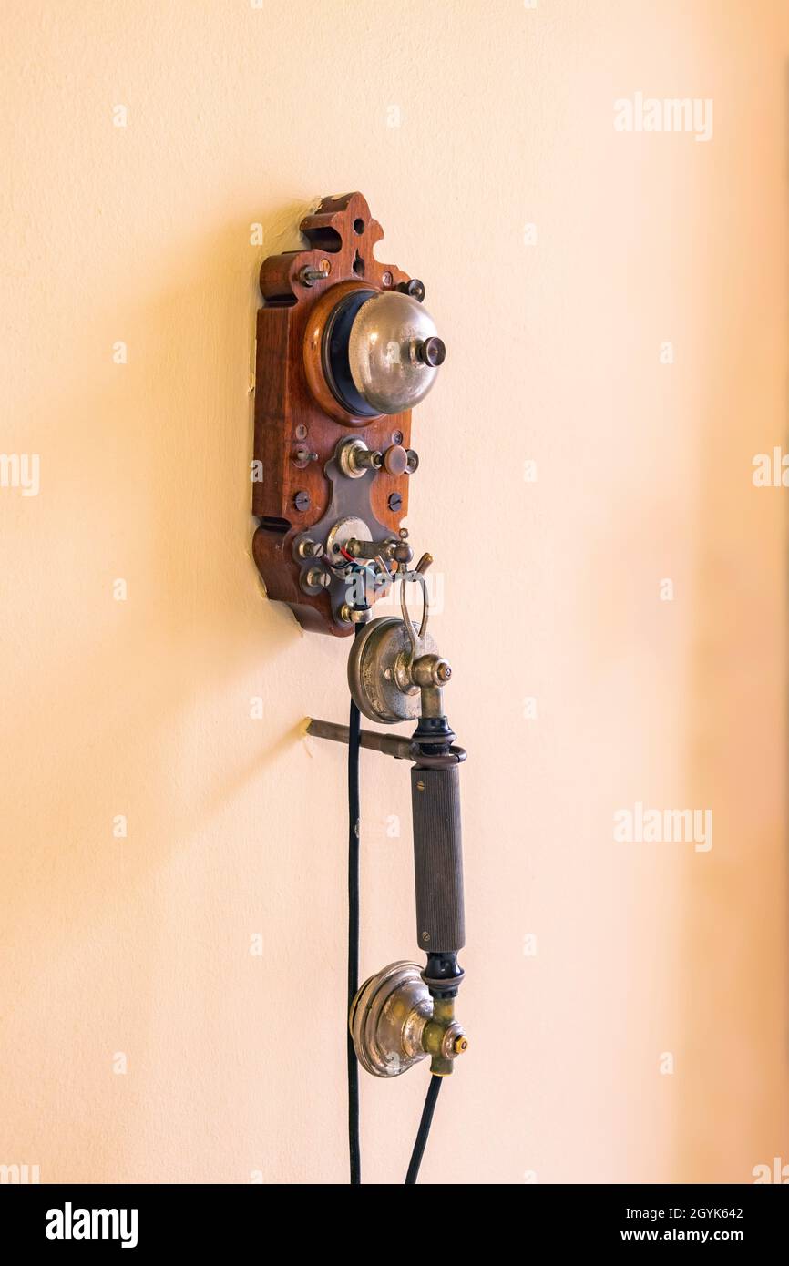 An einer gelben Wand hängt ein altes schnurgebundenes Telefon. Eines der ersten Telefone in Europa aus den 1880er Jahren Stockfoto