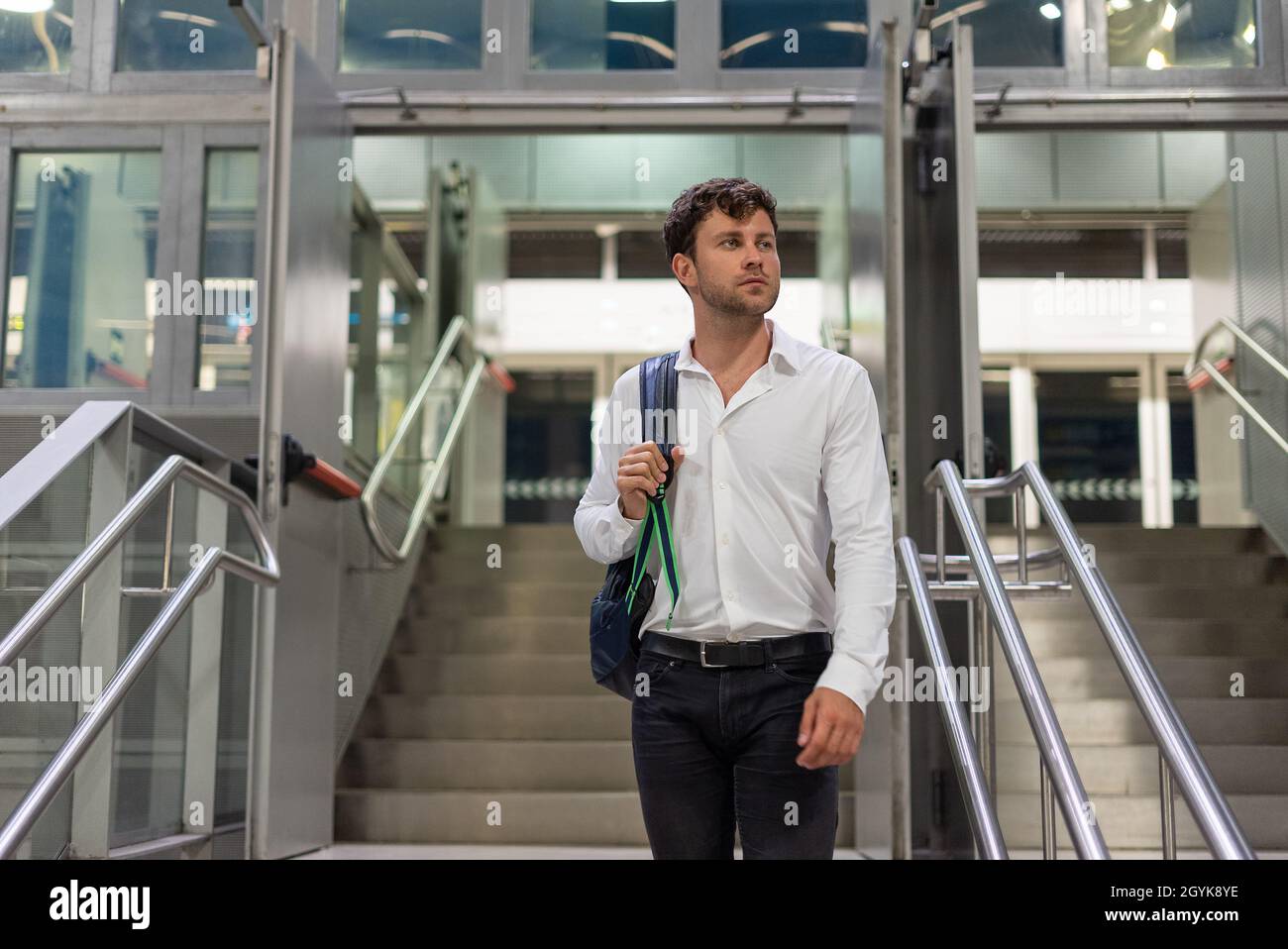 Männlicher Manager in eleganter, legerer Kleidung, die eine Tasche trägt und wegschaut, während er auf einer Geschäftsreise auf der Treppe auf dem Flughafen steht Stockfoto