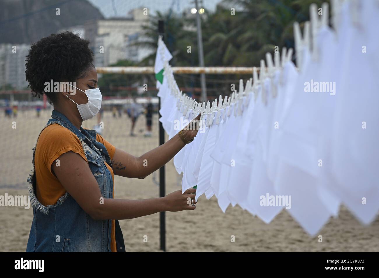 Rio De Janeiro, Brasilien. Okt. 2021. Eine Frau hängt weiße Taschentücher am Strand von Cocoba während einer Demonstration zum Gedenken an Menschen, die in Brasilien an Covid-19 gestorben sind. In Brasilien wurden fast 600,000 Todesfälle verzeichnet. Kredit: Andre Borges/dpa/Alamy Live Nachrichten Stockfoto
