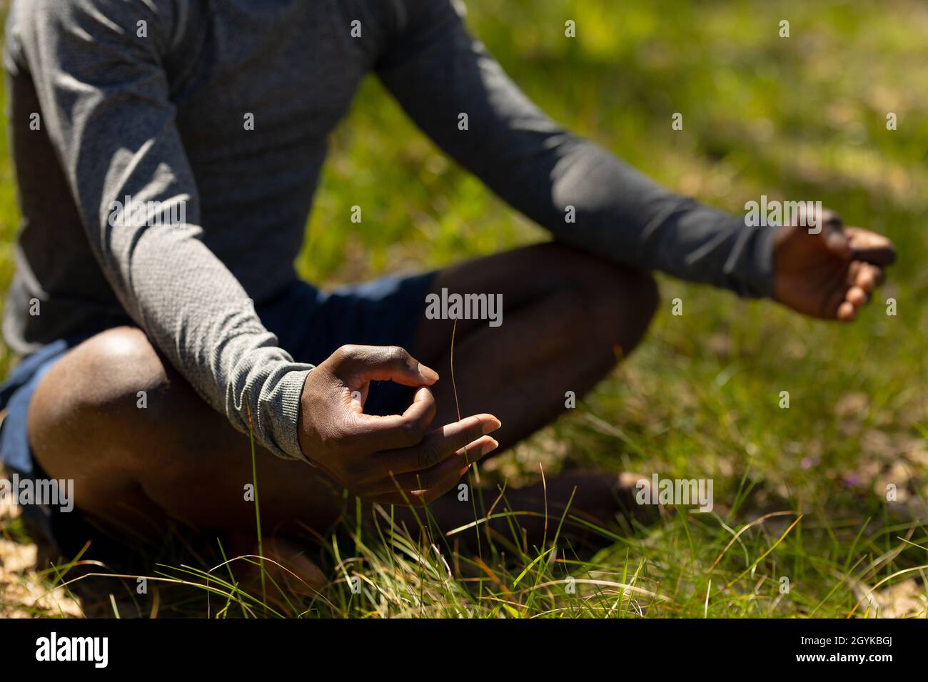 Entspannender afroamerikanischer Mann, der mit gekreuzten Beinen sitzt und auf dem Land meditiert Stockfoto