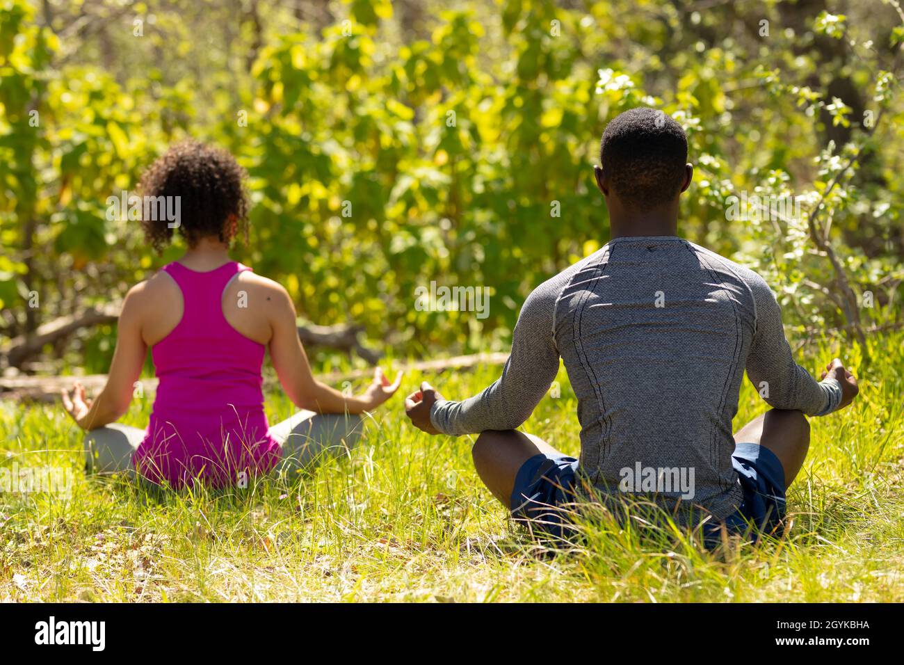 Entspannendes, vielfältiges Paar, das mit gekreuzten Beinen sitzt und auf dem Land meditiert Stockfoto
