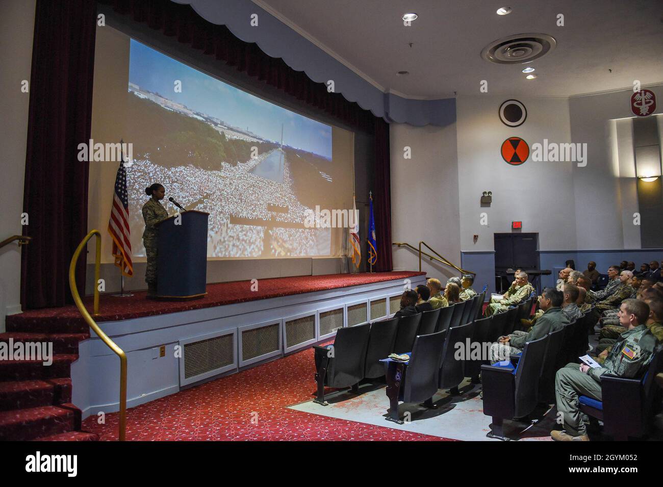 Airman 1st Class Muzan Elshiek, 627. Auszubildender der Logistik Readiness Squadron Supply, wartet darauf, weiter zu erzählen, während das Publikum ein Video über Martin Luther King Jr.'s Leben und seine Leistungen im McChord Theatre auf der Joint Base ansieht Lewis-McChord, Washington, 24. Januar 2020. Das Foto, das auf die Leinwand projiziert wurde, war der Marsch auf Washington für Arbeitsplätze und Freiheit, der am 23. August 1963 stattfand und an dem schätzungsweise 250,000 Menschen teilnahmen. (USA Luftwaffe Foto von Airman 1st Class Mikayla Heineck) Stockfoto