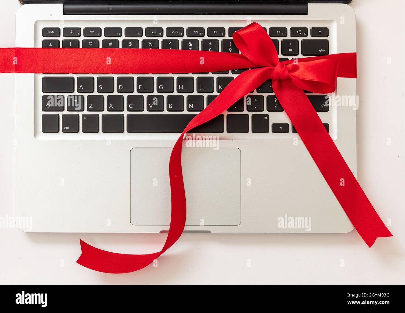 Laptop-Computer mit rotem Band Schleife, Digital-Gerät Weihnachtsgeschenk isoliert auf weißem Hintergrund. Valentinstag, Weihnachtsgeschenk, Draufsicht. Stockfoto