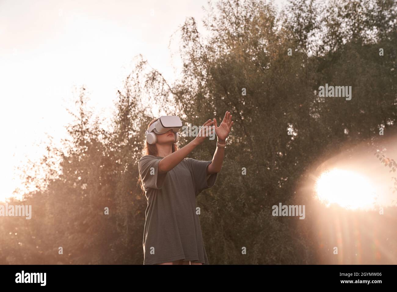 Ein Mädchen mit einer Virtual-Reality-Brille. Er reicht seine Hände an den Sonnenstrahl. Hochwertige Fotos Stockfoto