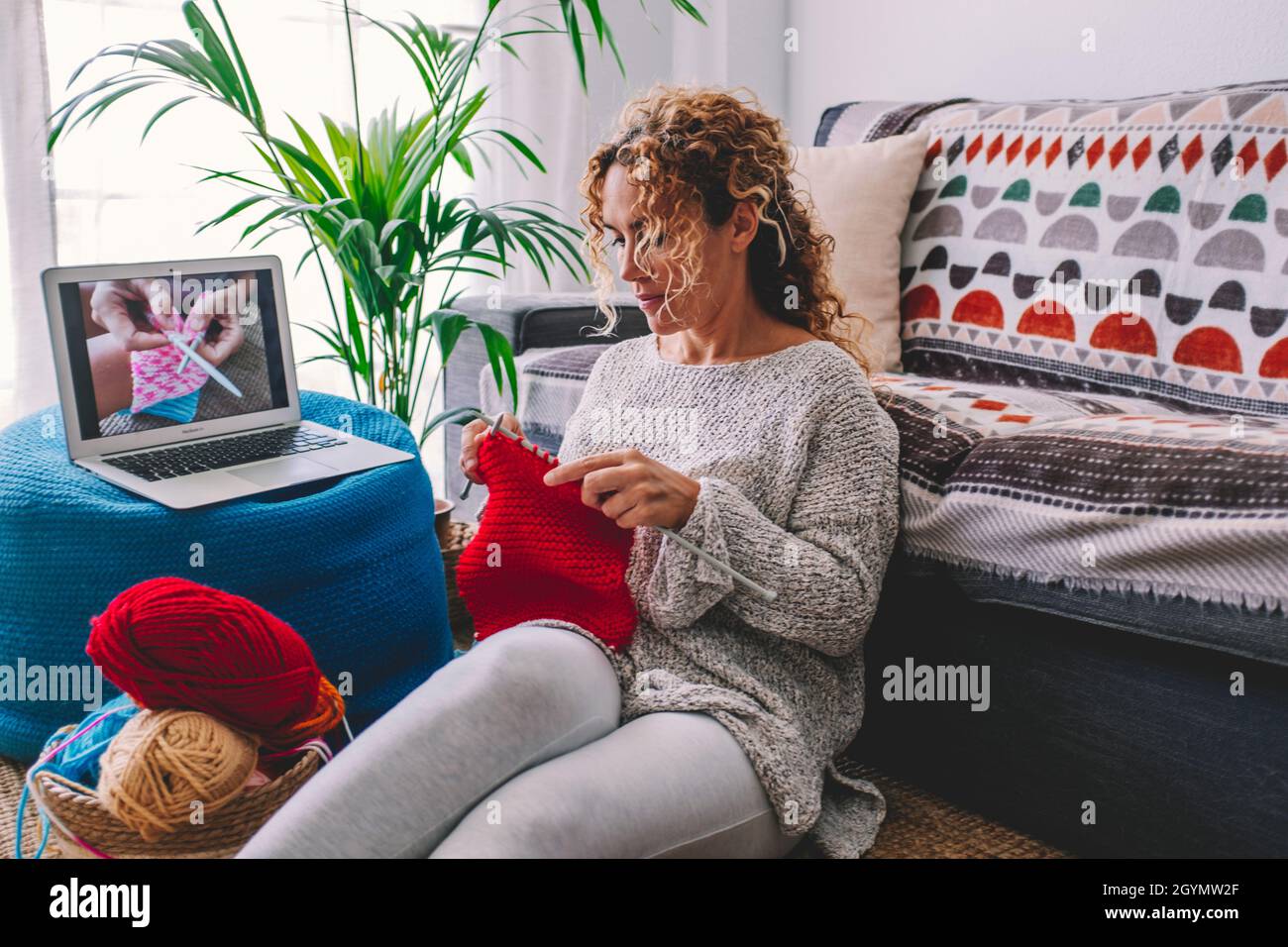 Gemütliche Strickfrau folgen Tutorial in gestrickten Winter warmen Pullover und im Pyjama genießt stricken Arbeit auf rot karierten karierten karierten Decke zu Hause in gemütlichen Wint Stockfoto