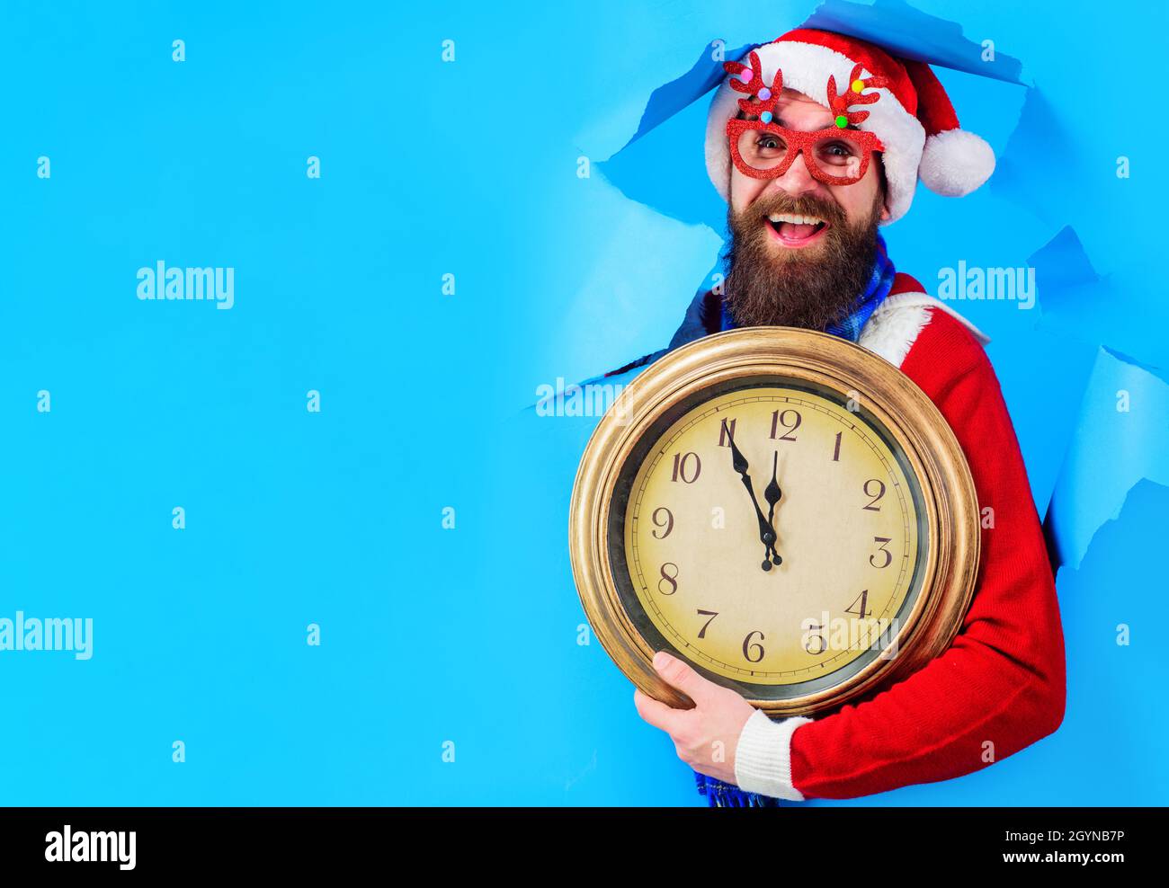 Countdown für das neue Jahr. Lächelnder Weihnachtsmann mit Vintage-Uhr schaut durch das Papierloch. Vorbereitung auf Weihnachten. Speicherplatz kopieren, Stockfoto