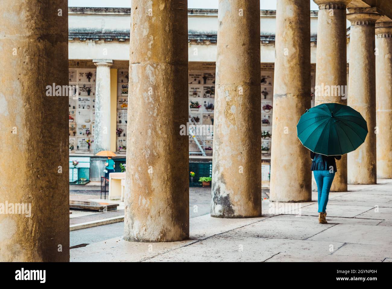An einem regnerischen Tag laufen Menschen mit Sonnenschirmen durch einen Friedhof. Stockfoto