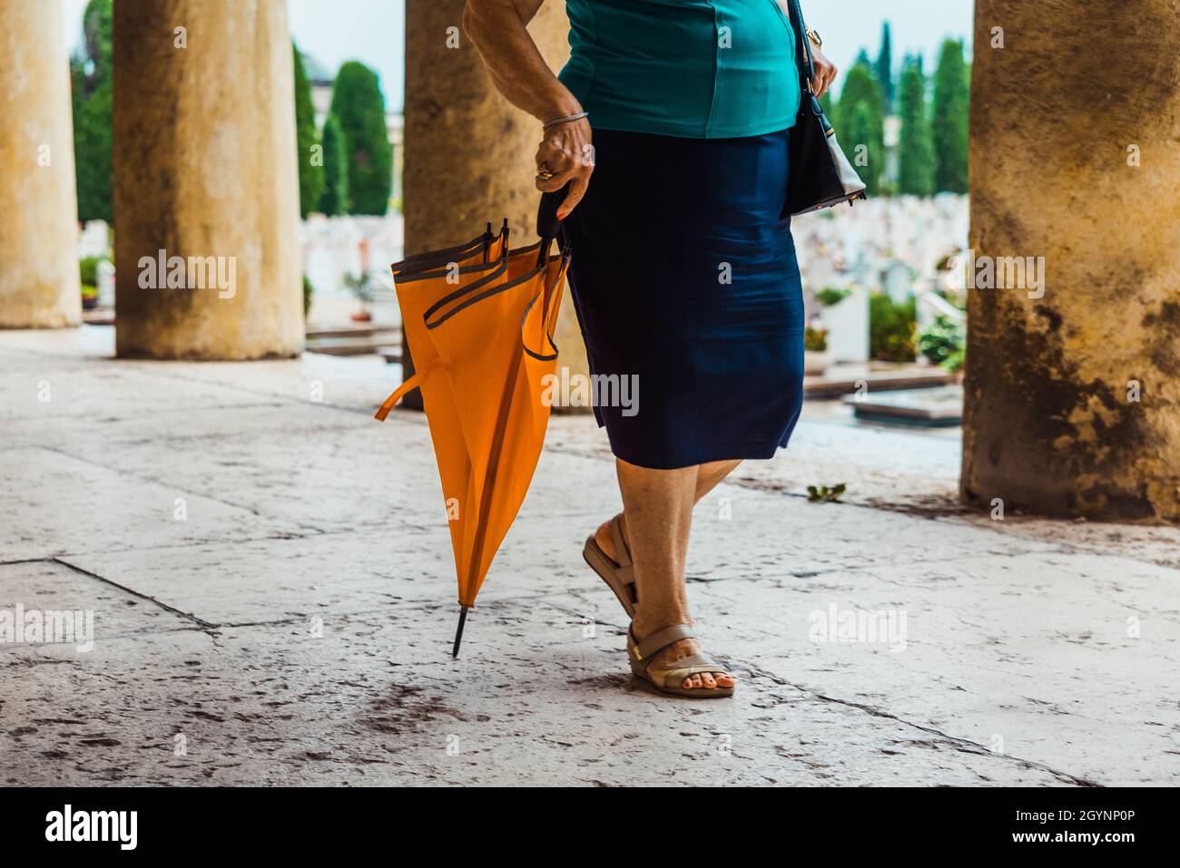An einem regnerischen Tag laufen Menschen mit Sonnenschirmen durch einen Friedhof. Stockfoto