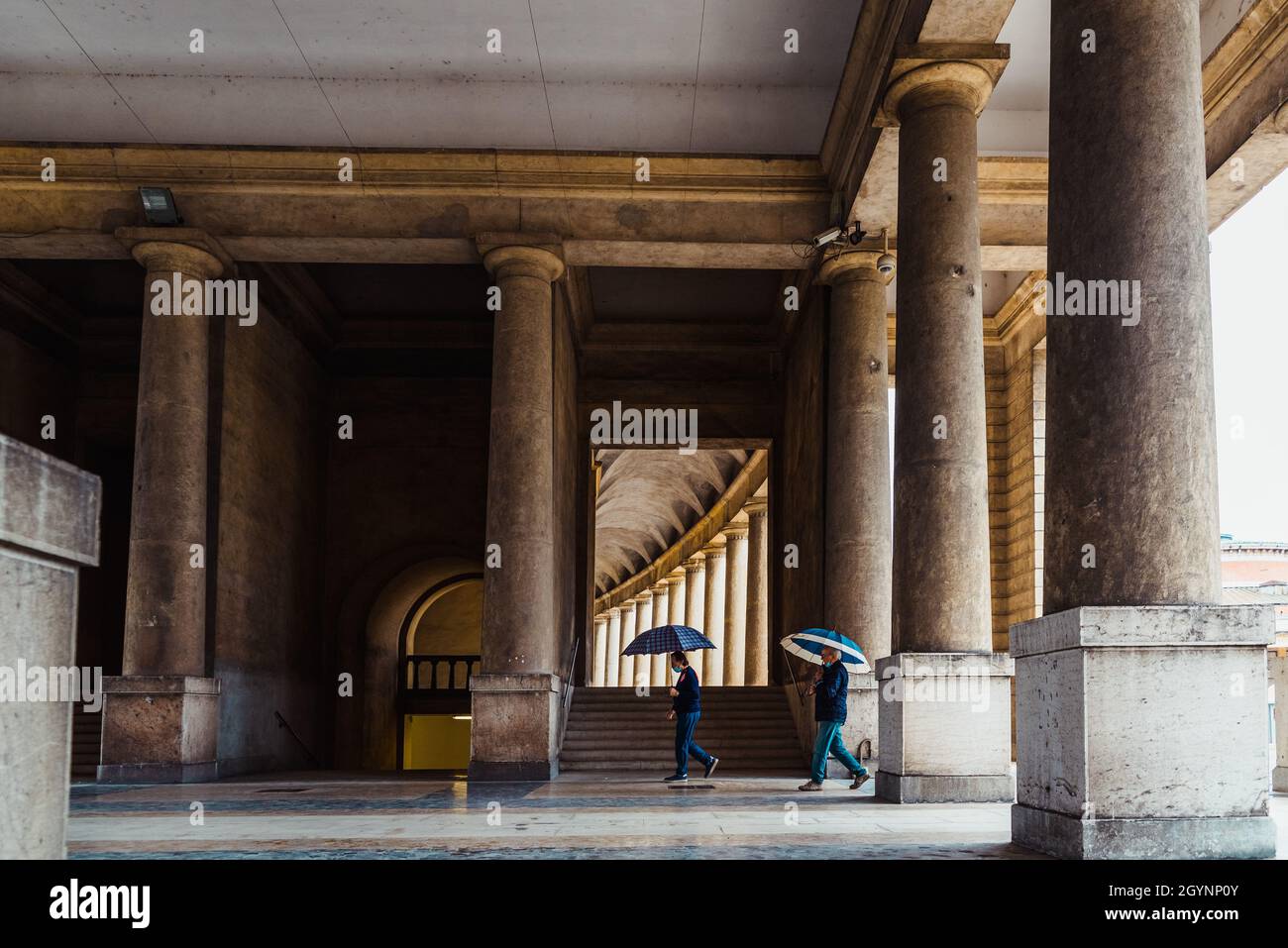 An einem regnerischen Tag laufen Menschen mit Sonnenschirmen durch einen Friedhof. Stockfoto