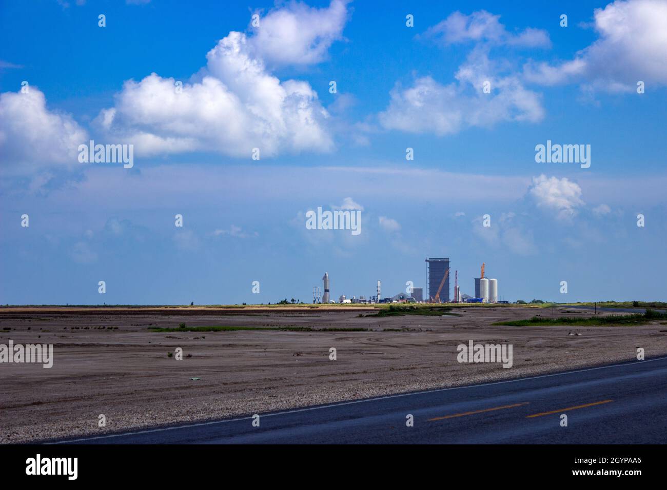 SpaceX Starbase breitet sich unter wabenden, geschwollenen, weißen Wolken aus. Der Hochregallager und der Vorbau sind auf dem Gelände in der Nähe von Brownsville, TX, zu sehen. Stockfoto