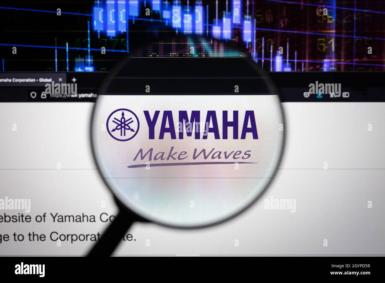 Yamaha-Firmenlogo auf einer Website mit verschwommenen Börsenentwicklungen im Hintergrund, auf einem Computerbildschirm durch eine Lupe gesehen Stockfoto