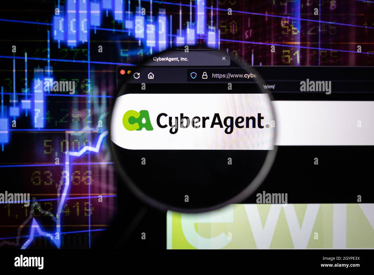 Das Unternehmenslogo von Cyber Agent auf einer Website mit verschwommenen Börsengrafiken im Hintergrund, die auf einem Computerbildschirm durch eine Lupe gesehen werden. Stockfoto