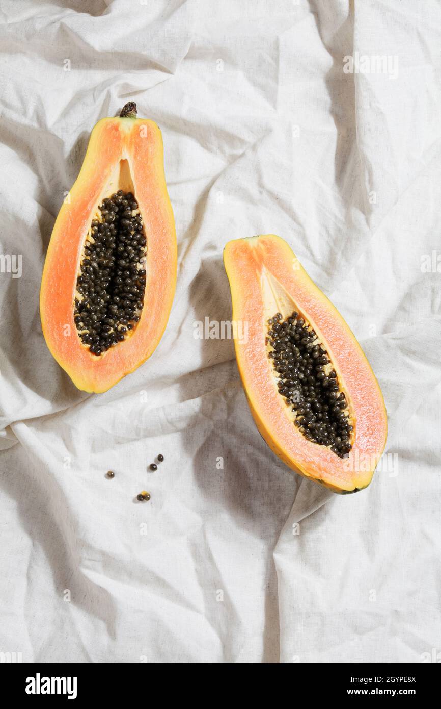 Kreatives Food-Konzept mit halber Papaya auf zerknittertem grauem Leinen. Flach Lay Draufsicht. Minimalistisch bunte Natur Hintergrund. Stockfoto
