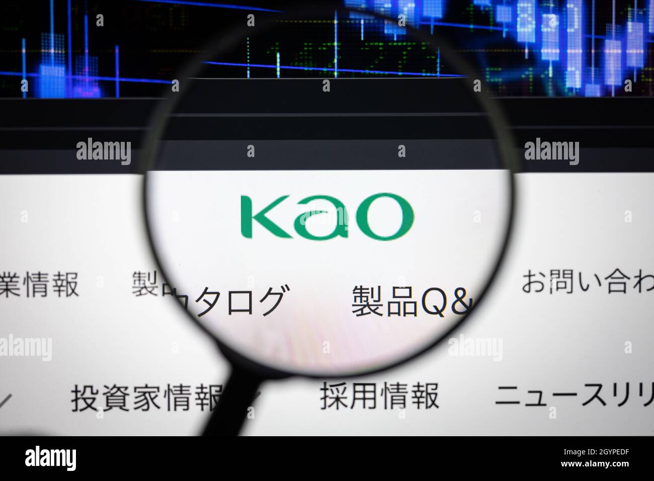 KAO Firmenlogo auf einer Website mit verschwommenen Börsengrafiken im Hintergrund, die auf einem Computerbildschirm durch eine Lupe gesehen werden. Stockfoto