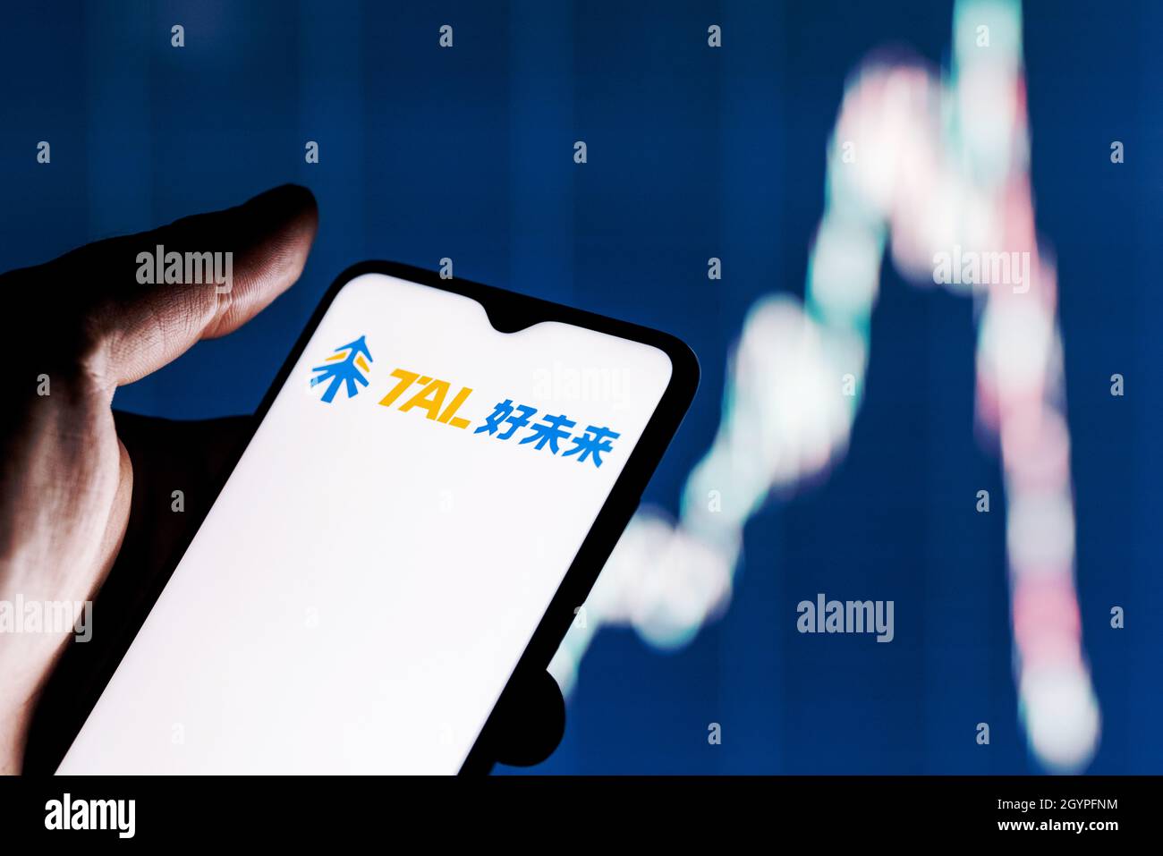 Ein Smartphone mit dem Tal-Logo in der Hand. Aktiendiagramm im Hintergrund. Stockfoto