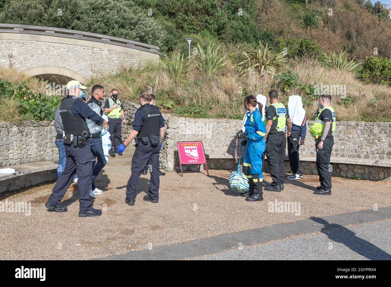 Polizeibeamte und eine Küstenwache mit kürzlich eingetroffenen Einwanderern an der Strandpromenade von Folkestone, Kent. Stockfoto