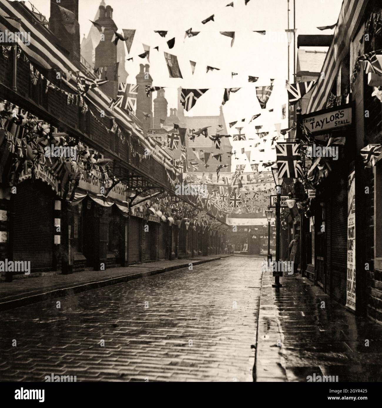 The Shambles in Huddersfield, Yorkshire, England im Jahr 1937. Schilder für „Tripe Taylor’s Stall“ und „Fish Chips Pies Peas“ (rechts) sind typisch für die Straße in der englischen Marktstadt in den 1930er Jahren Flaggen, Fahnen und Banner feiern die Krönung des britischen Monarchen König George VI. Vintage-Fotografie aus privater Sammlung. Stockfoto