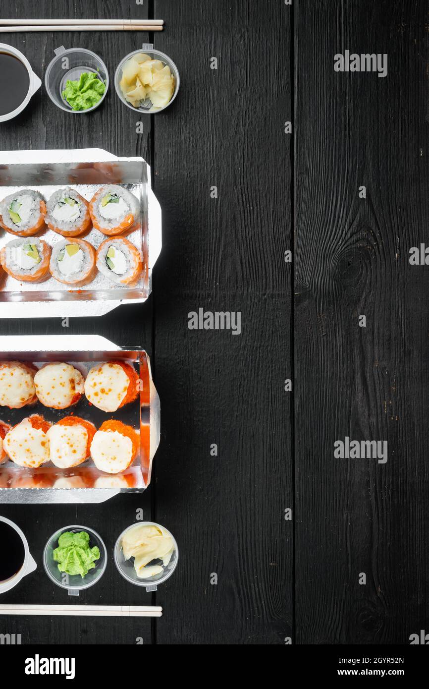 Sushi-Rollen im Takeaway-Container-Set, auf schwarzem Holztischhintergrund, Draufsicht flach liegend, mit Copyspace und Platz für Text Stockfoto