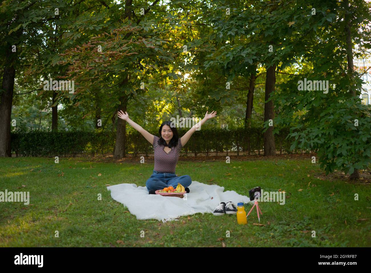Herbstpicknick im Stadtpark - Lifestyle-Porträt einer jungen glücklichen und schönen asiatischen koreanischen Frau, die Gras mit Decke und Obstkorb sitzt und die r Stockfoto