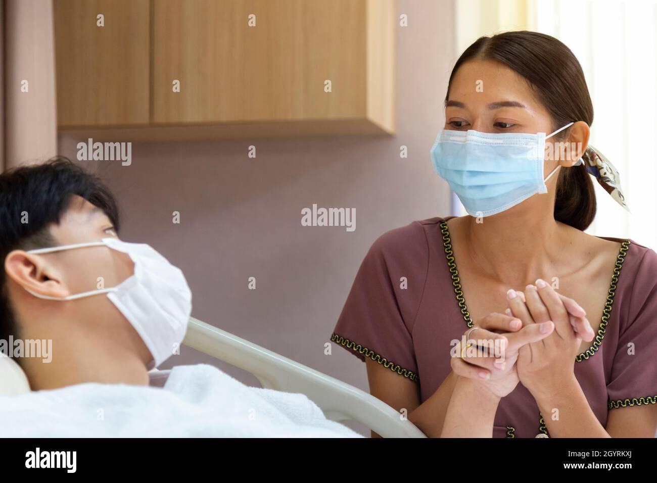 Beunruhigende asiatische Mutter hält Hand und kümmern Patienten Teenager Sohn trägt eine schützende Gesichtsmaske nach der Erholung von covid Quarantäne-Behandlung in h Stockfoto
