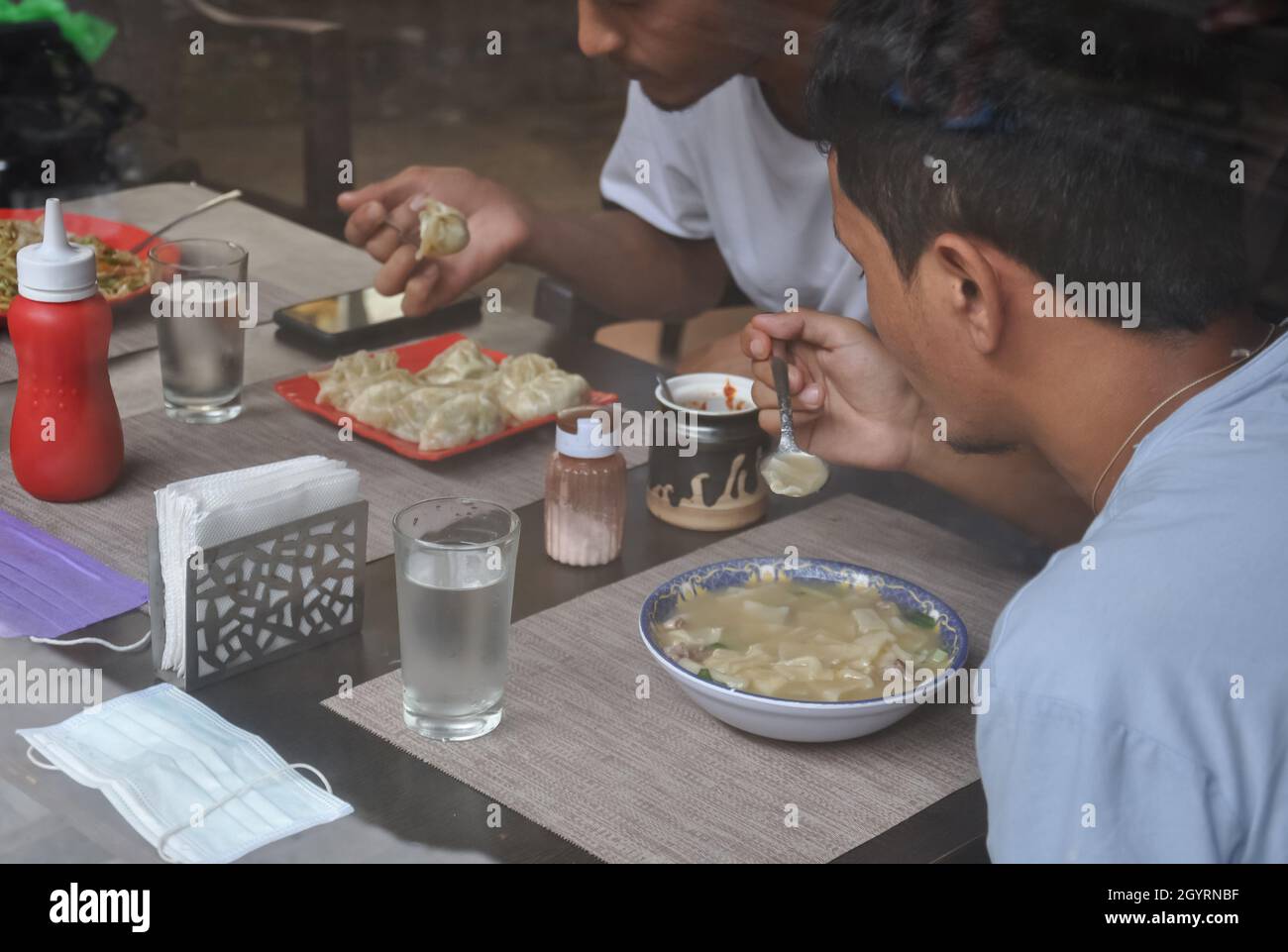 Selektiver Fokus von zwei jungen Jungs, die tibetisches Essen im Innencafe durch das Fenster gesehen essen Stockfoto