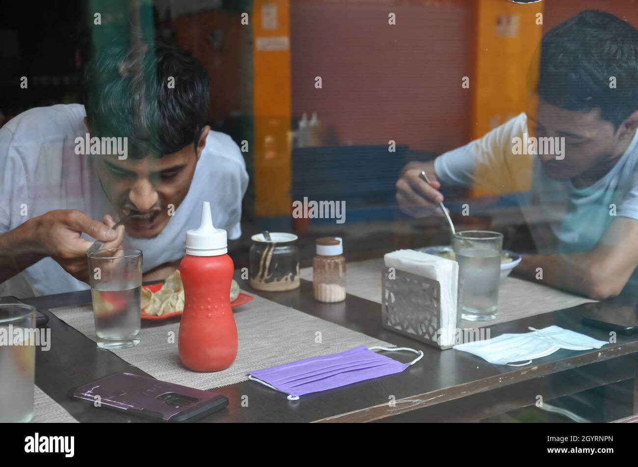 Zwei junge Leute essen Fast Food im Cafe im Innenbereich, das durch das Fenster gesehen wird Stockfoto