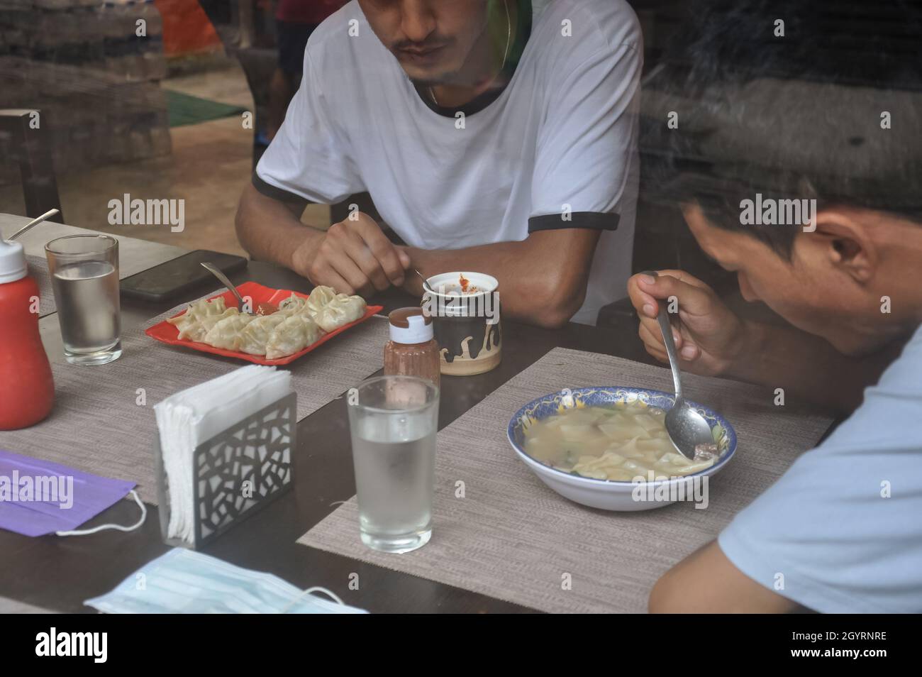 Selektiver Fokus von zwei jungen Jungs, die tibetisches Essen im Innencafe durch das Fenster gesehen essen Stockfoto