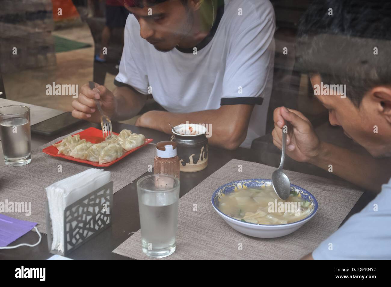 Zwei männliche Freunde essen tibetisches Essen in einem Café, das durch das Fenster gesehen wird Stockfoto