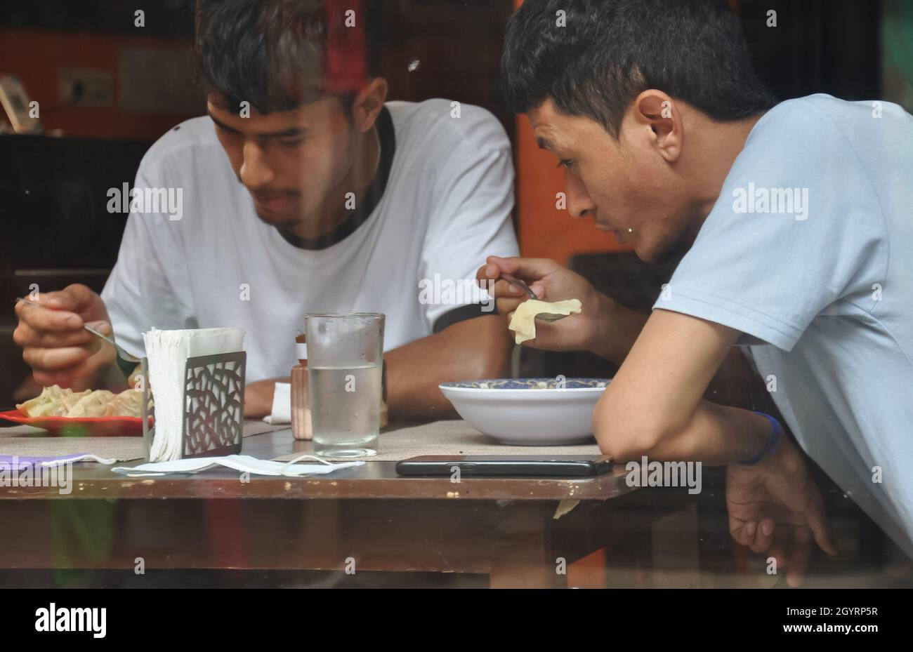 Zwei junge Leute essen Fast Food im Cafe im Innenbereich, das durch das Fenster gesehen wird Stockfoto