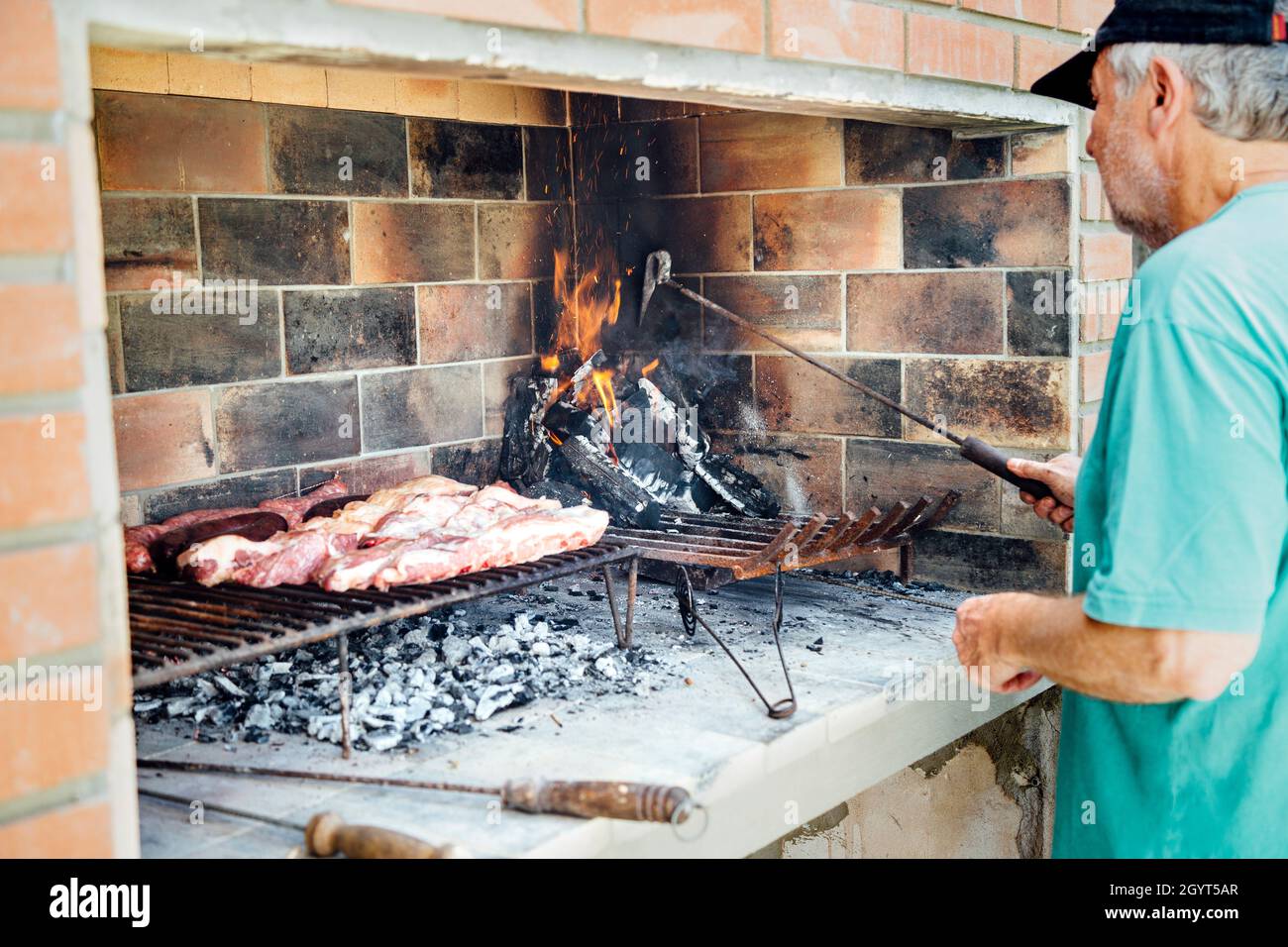 Argentinischer reifer Mann, der auf dem Grill seines Hauses gegrillt wird. Traditionelles Mittagessen am Wochenende. Stockfoto