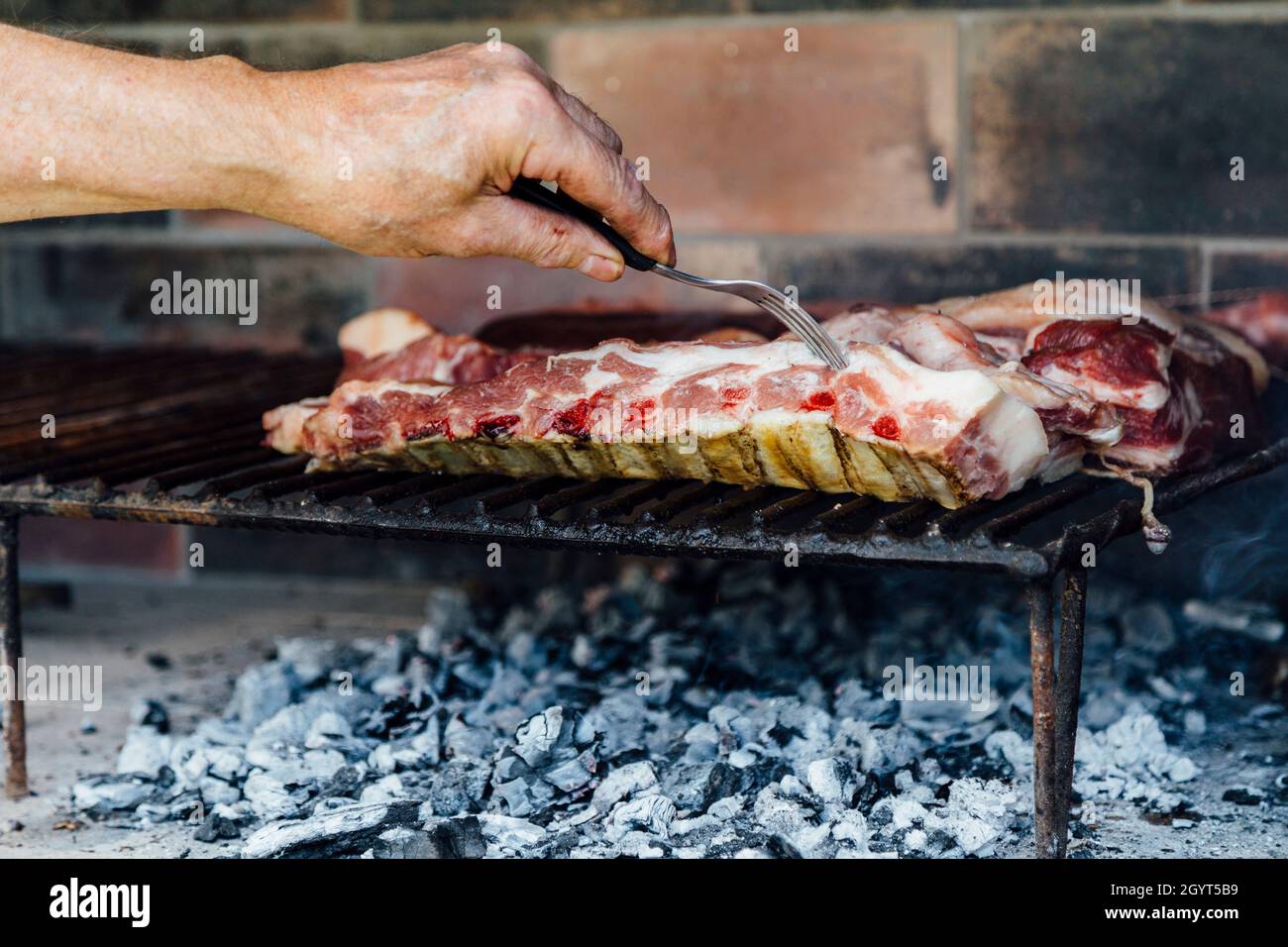 Die Hand eines reifen Mannes beim Grillen. Er prodding das Fleisch mit einer Gabel. Stockfoto