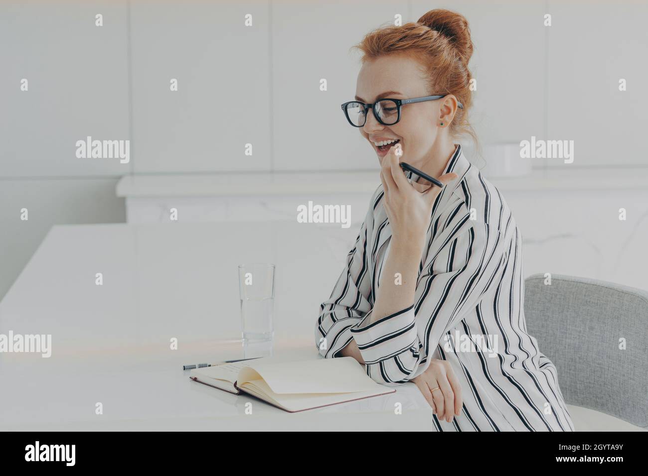 Lächelnde Frau, die mobil hält und zu Hause mit dem virtuellen digitalen Spracherkennungsassistenten spricht Stockfoto