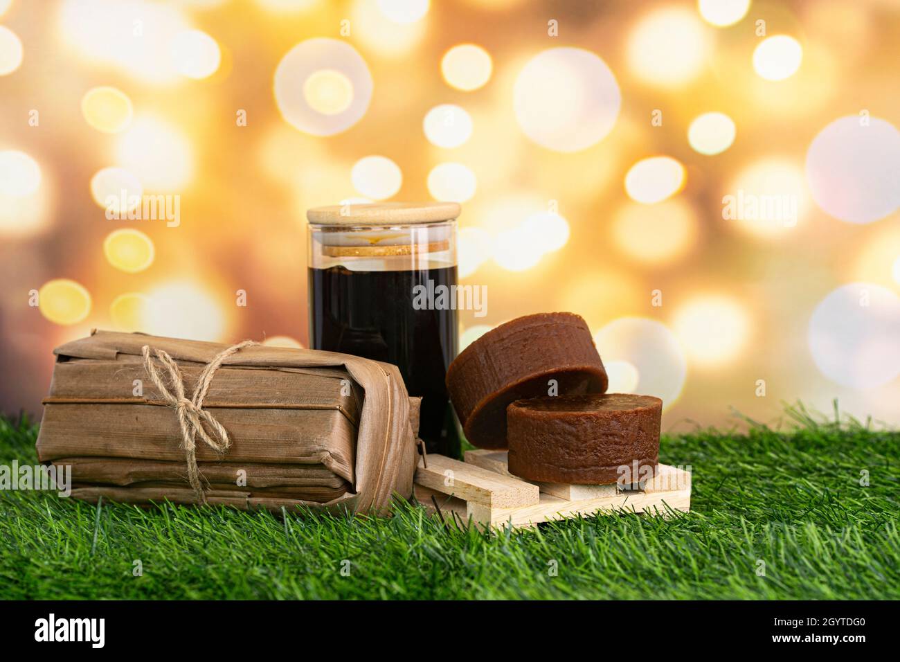 Eine Verpackung von Palmzucker mit einem Glas verflüssigter Version. Traditionell werden sie mit trockenen Kokosnussblättern verpackt. Selektive Fokuspunkte. Verschwommener Backgr Stockfoto