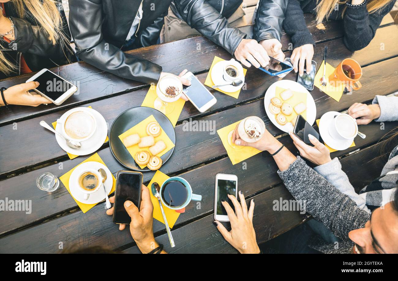 Draufsicht auf die Hände von Freunden, die Cappuccino im Café trinken - die Leute, die Spaß haben, gemeinsam Kuchen zu essen und das Handy im Café zu benutzen Stockfoto