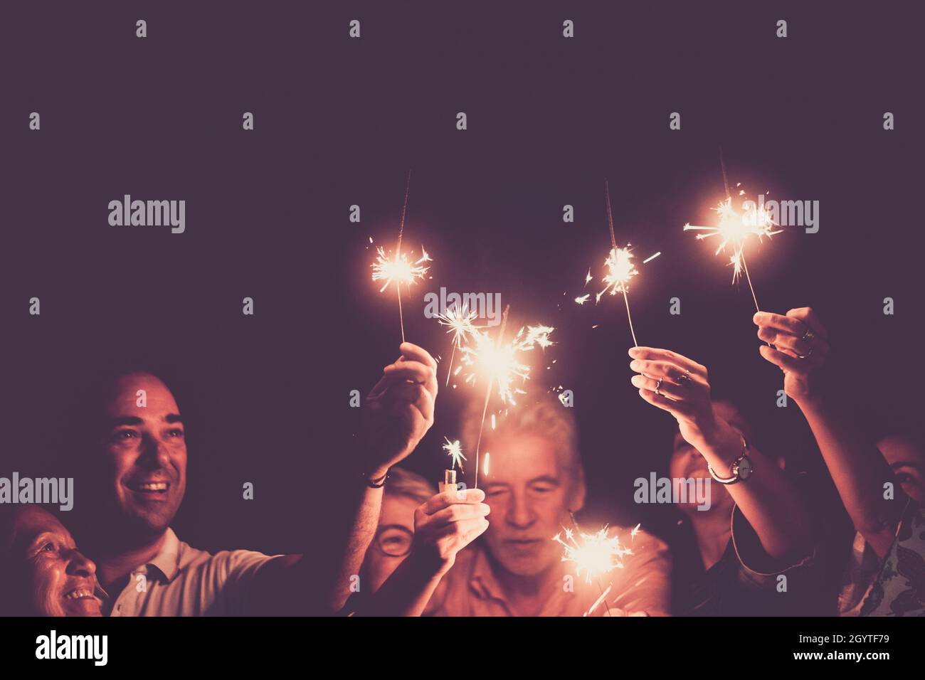 Familie feiert halten brennende funkelt mit erhobenen Armen. Eine Gruppe von Familien mit mehreren Generationen, die einen Geburtstag, ein Jubiläum oder ein neues Jahr feiern. Männer Stockfoto