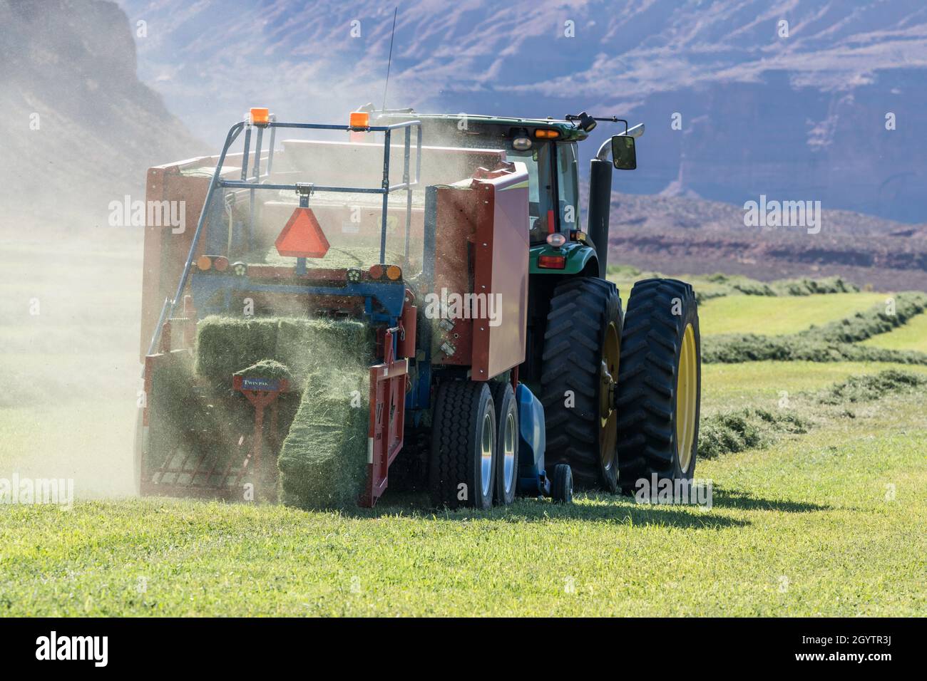 Heuballenpressen mit einem John Deere Traktor 7930 und einer GPT Twin Pak Ballenpresse auf einer Ranch im Süden von Utah. Stockfoto