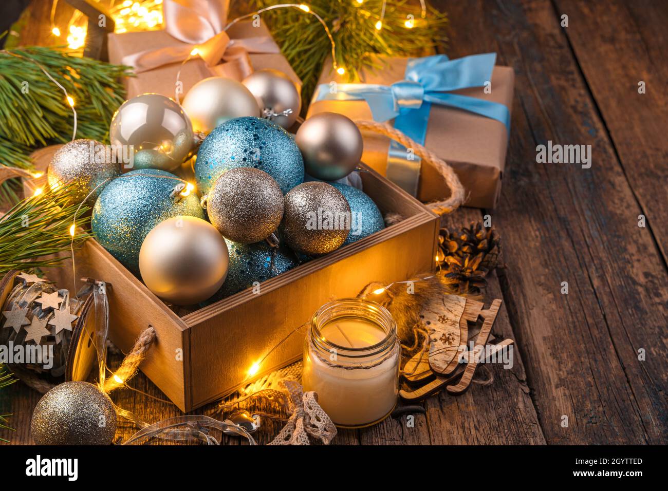 Eine Schachtel mit goldenen und blauen Weihnachtskugeln in Christbaumzweigen mit leuchtenden Lichtern. Das Konzept von Weihnachten und Neujahr. Stockfoto