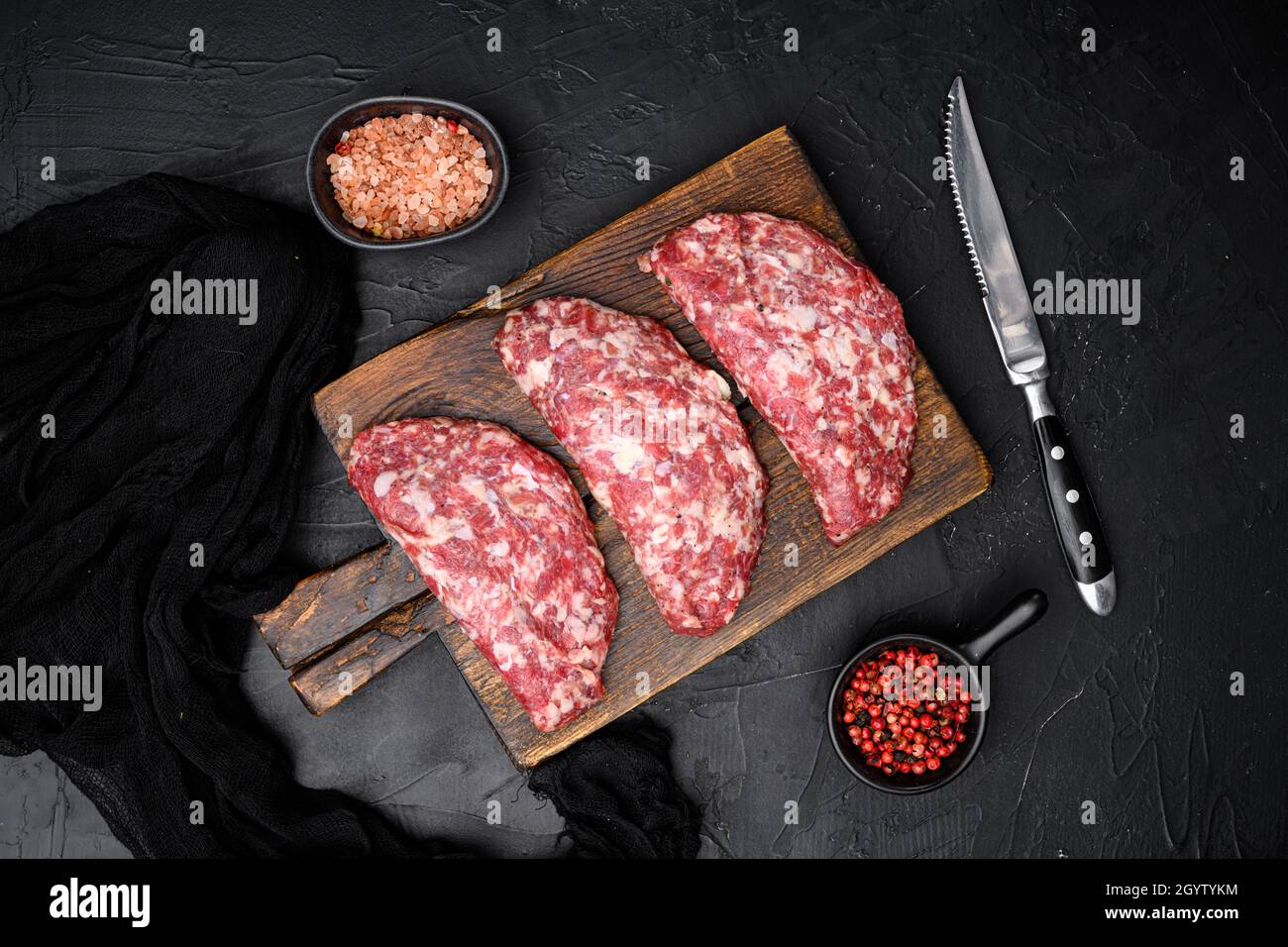 Hacksteaks aus rohem Fleisch gemahlen. Fleischpatty-Set, auf schwarzem dunklen Steintisch-Hintergrund, Draufsicht flach liegend Stockfoto