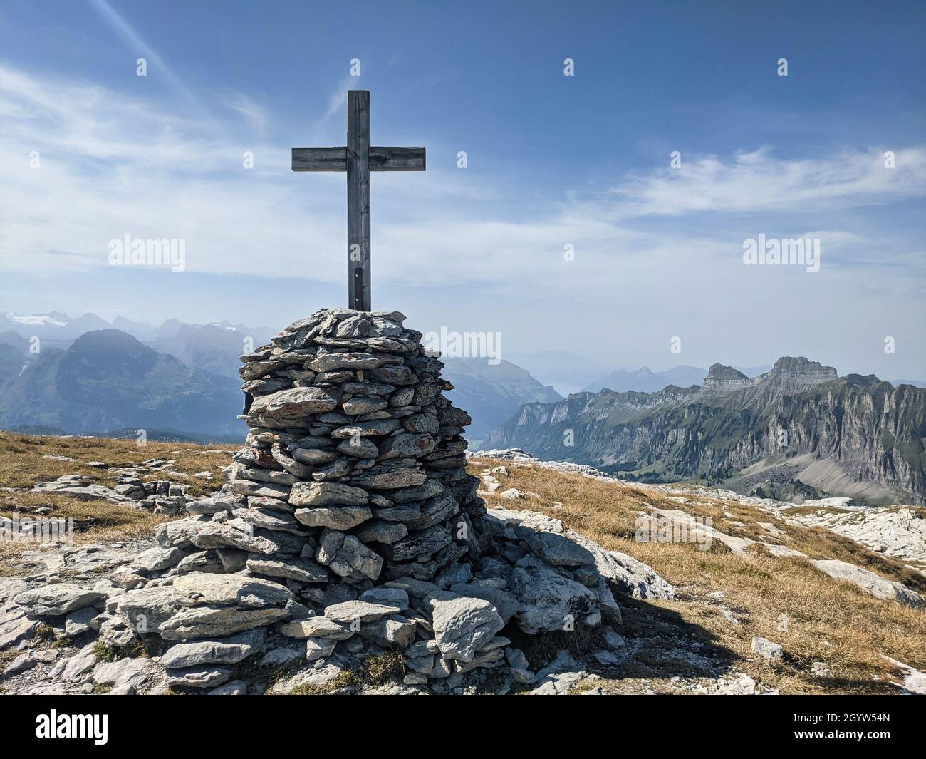 Gipfelkreuz in den schweizer Bergen mit Blick auf die Berggipfel und wunderschöne Almwiesen. Schönes Wanderwetter. Stockfoto