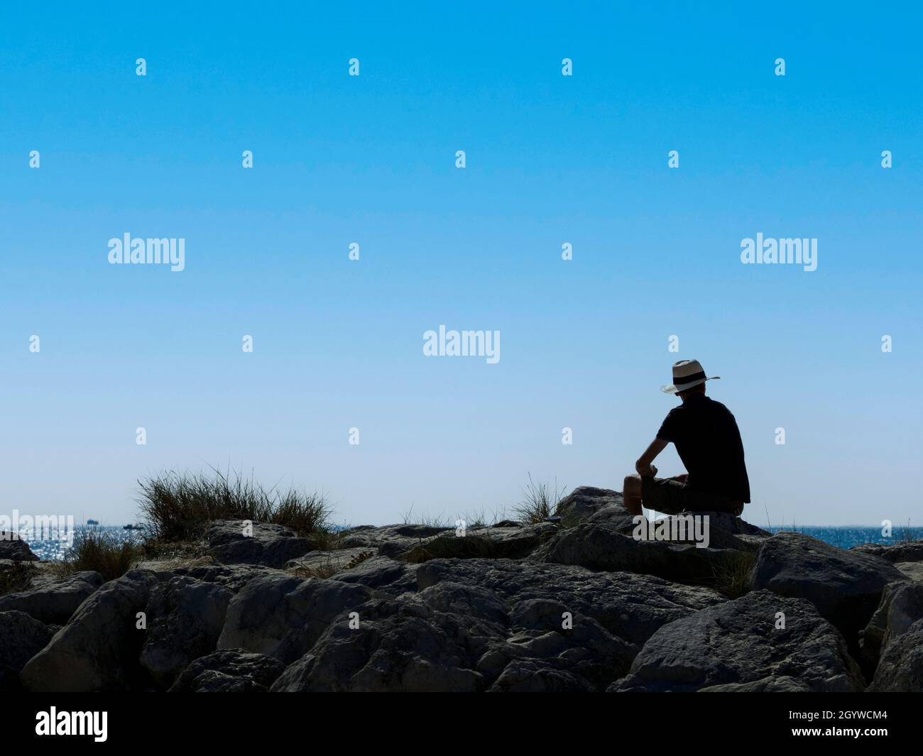 Mann in einem Hut saß auf Felsen und blickte aufs Meer, Mudeford, Spit, Hengistbury Head, Dorset, VEREINIGTES KÖNIGREICH, Stockfoto