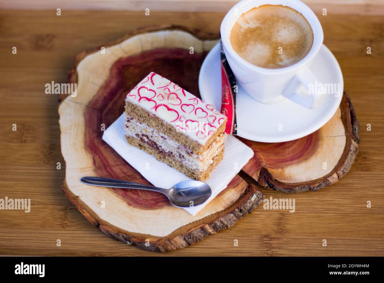 Leckere Tortenscheibe mit Cremefüllung und Herzdekor auf der Oberseite mit Kaffee auf dem Kirschtafel. Kaffeepause Stockfoto