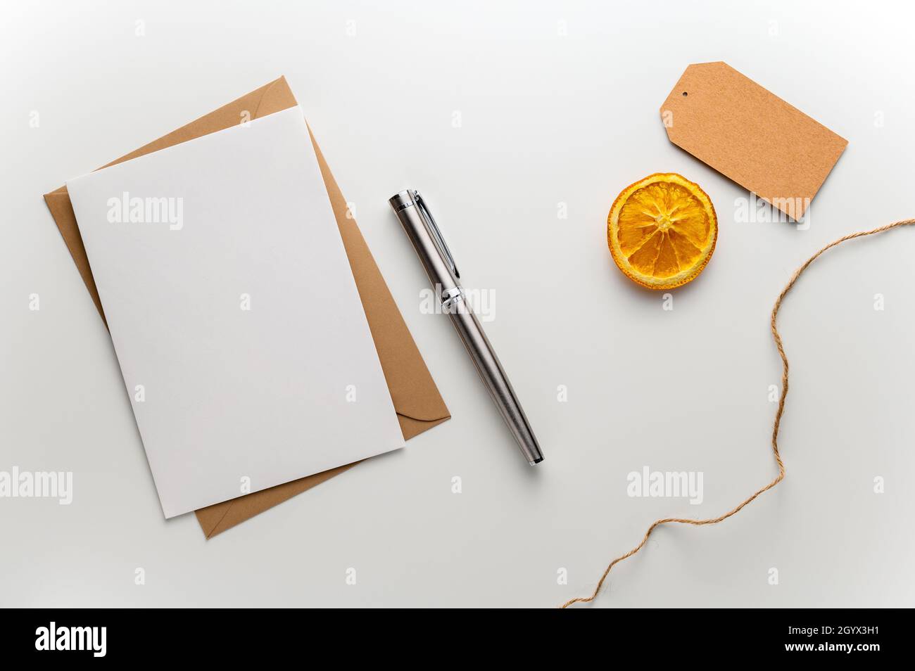 Weihnachtskarte mit Geschenkanhänger mit Bastelumschlag, Füllfederhalter und einem Stück getrockneten Orangen auf einem sauberen weißen Schreibtisch. Stockfoto