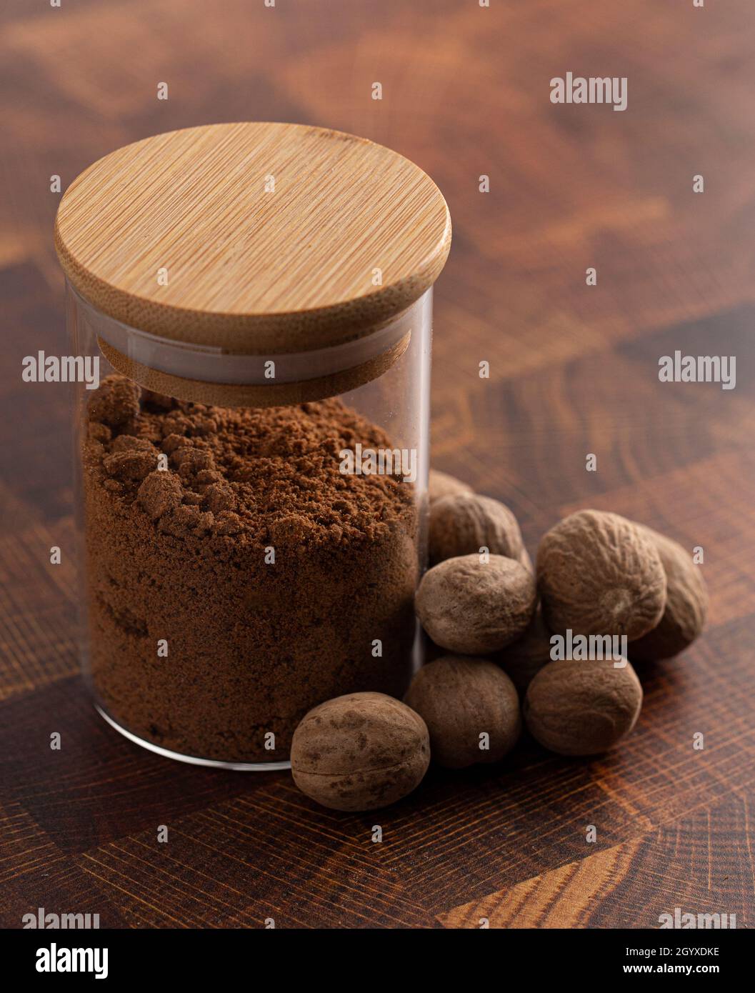 Glas gemahlener Muskatnuss und ganzer Muskatnuss auf einem Holztisch Stockfoto